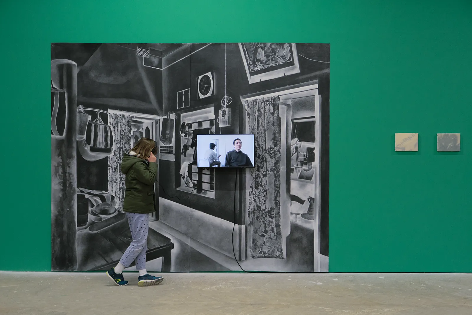 Installation view of Turning Back, a large charcoal drawing of an interior domestic space with a video screen installed on top of the drawing.