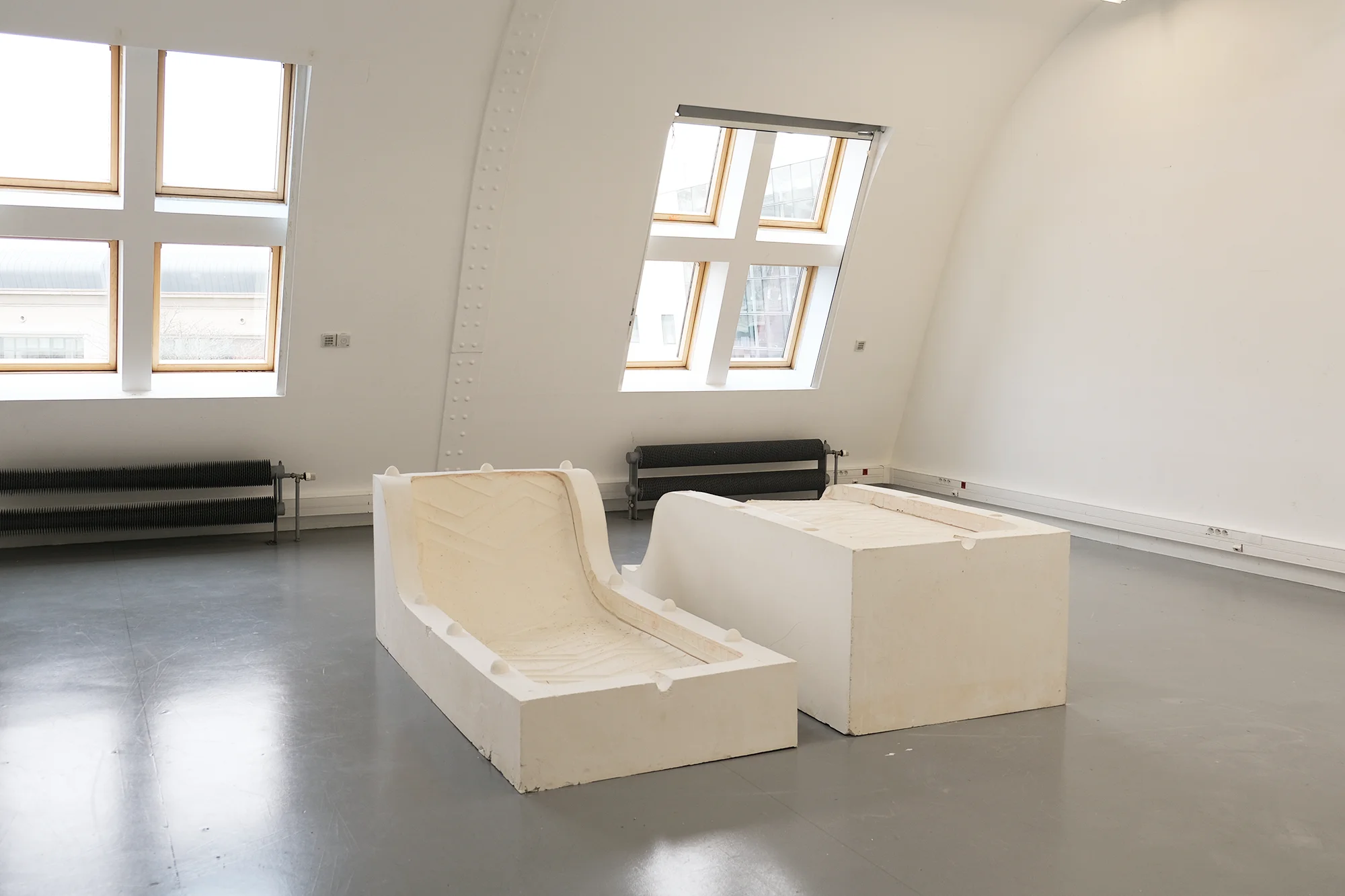 Exhibition view of La courbe, showing the plaster mould of a curved mattress within a gallery space. The work addresses bodily adaptation, spatial restriction and urban conditions of shelter.