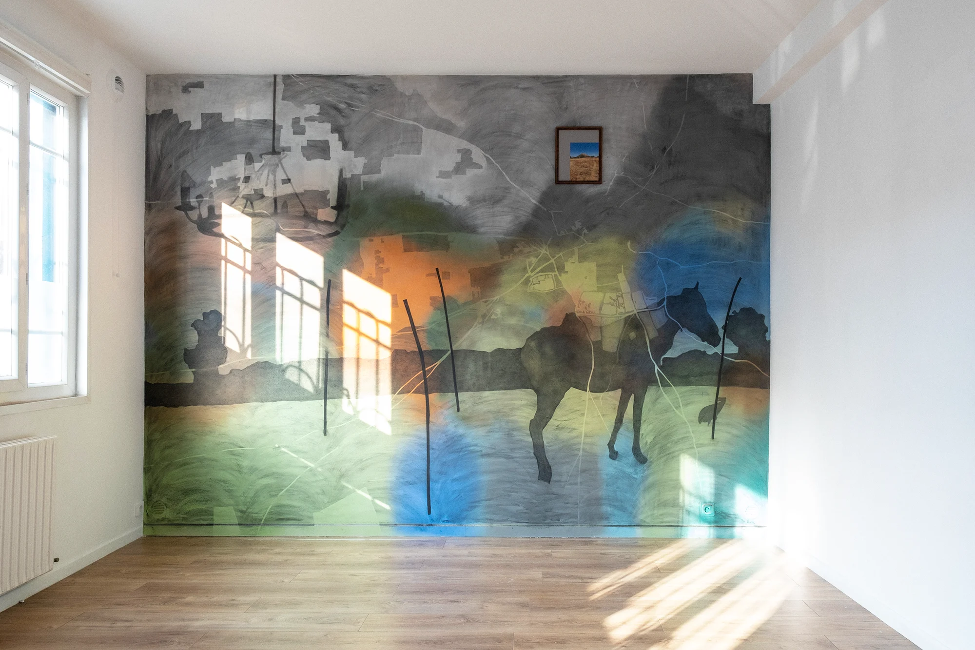 Aniruddha Biswas, Reconnecting…, 2025, wall painting with charcoal and aerosol acrylic at Maison Rester. Étranger, showing layered landscapes, silhouettes, colour fields and a framed photograph.